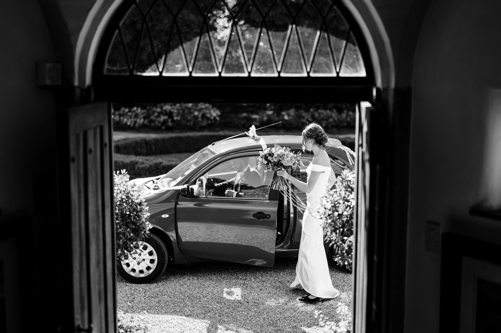 Voewood Bride entering car, holding bouquet, black and white photo.