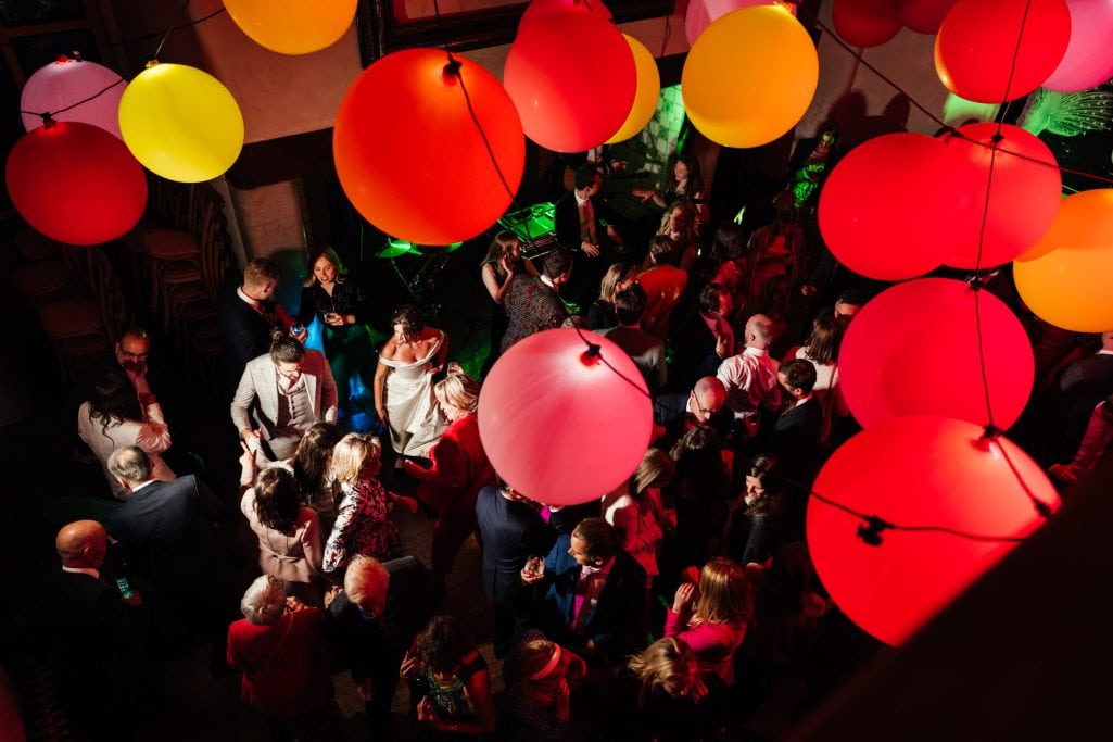 Vibrant party with colorful balloons and crowd dancing.