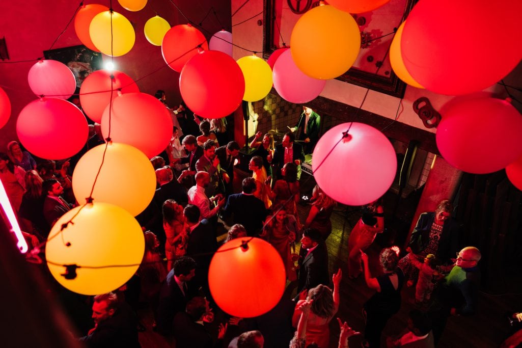 Vibrant Voewood wedding party with colorful hanging balloons and dancing people.