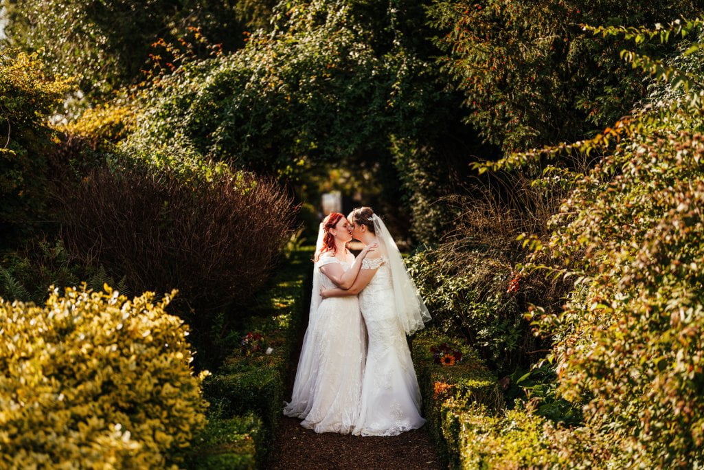 Two brides embracing in sunlit garden