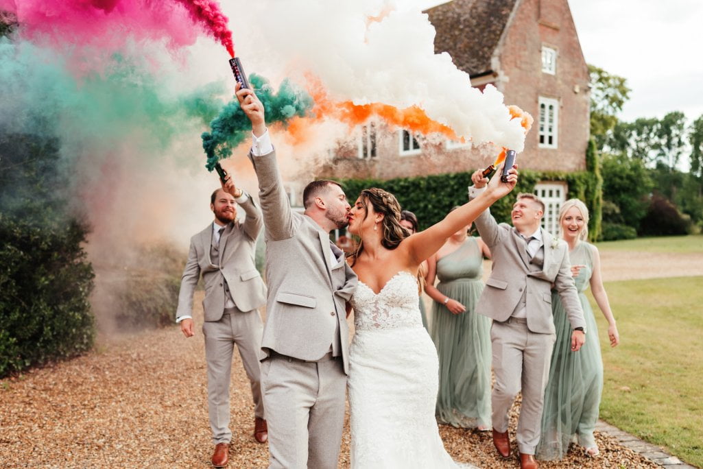 Bride, groom, guests with colourful smoke flares, joyful wedding.