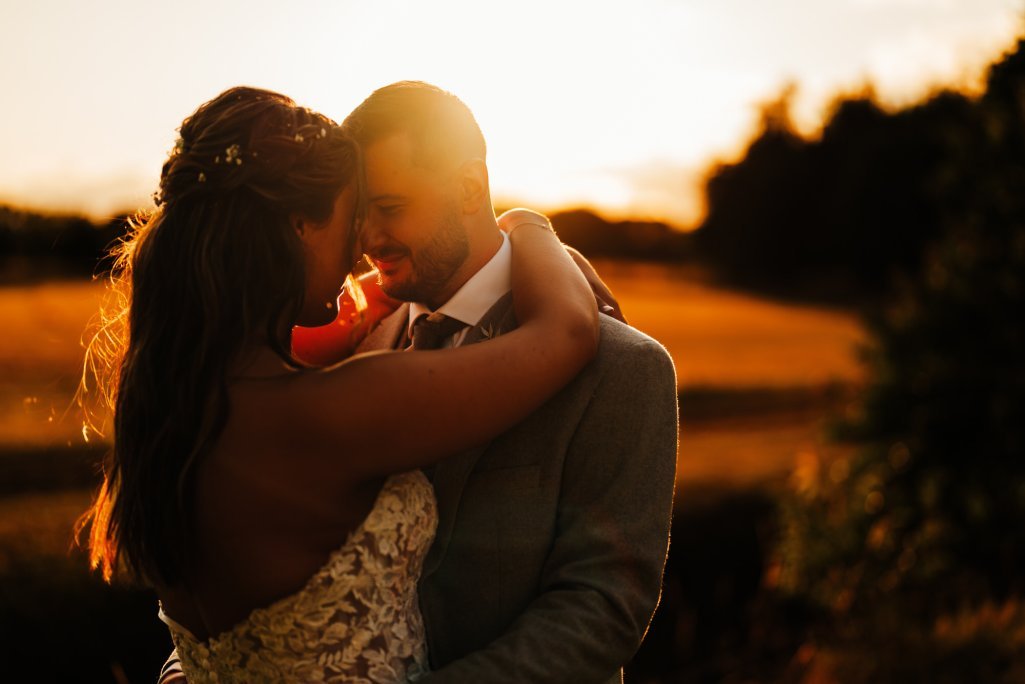 Couple embracing in sunset light at wedding.