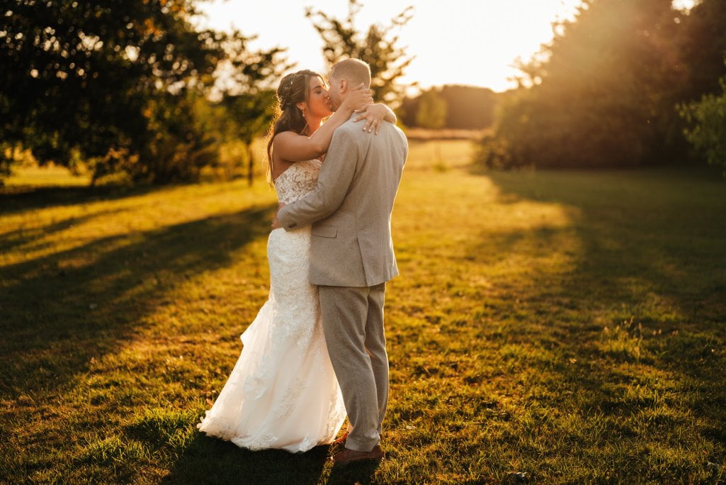 Bride and groom embracing outdoors at sunset.