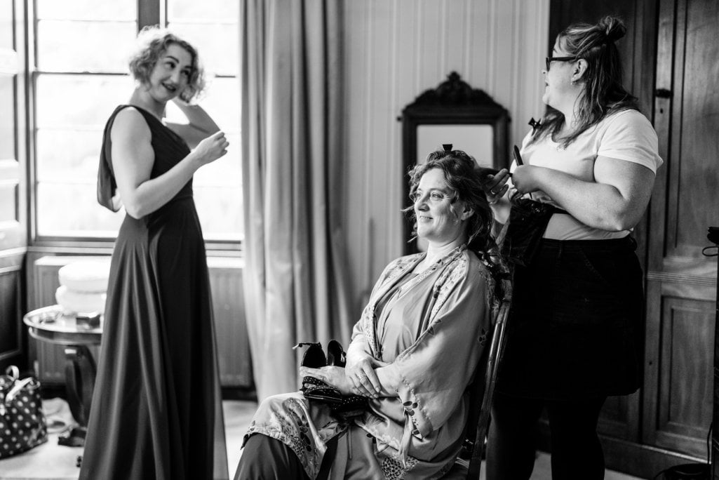 Bridal preparation with hairstyling and smiling attendant.
