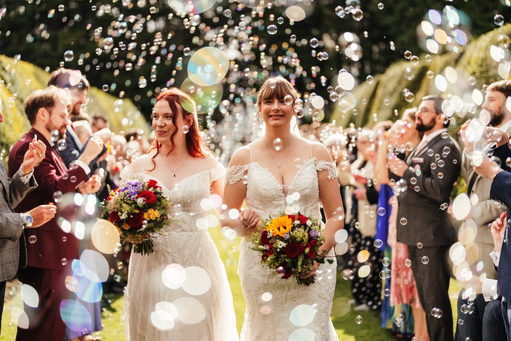 Two brides with bouquets at bubble-filled wedding ceremony.