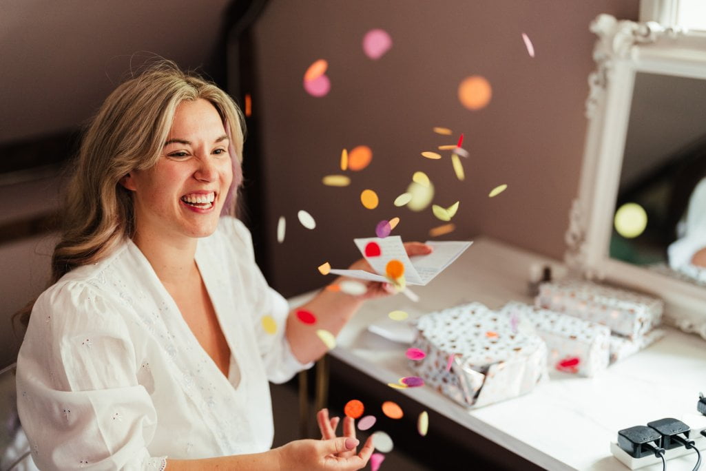 Woman laughing with confetti and letter at table.