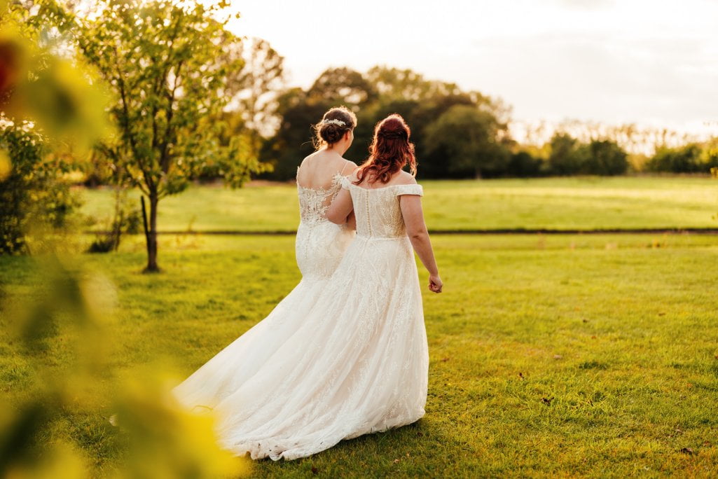 Two brides holding hands in sunset-lit field