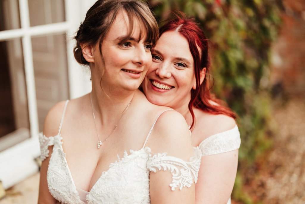 Two brides smiling in wedding gowns outdoors