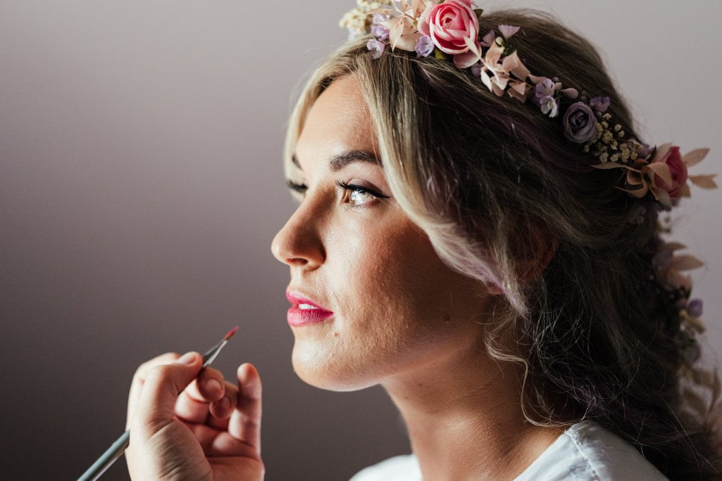 Bride getting makeup done with floral headpiece.