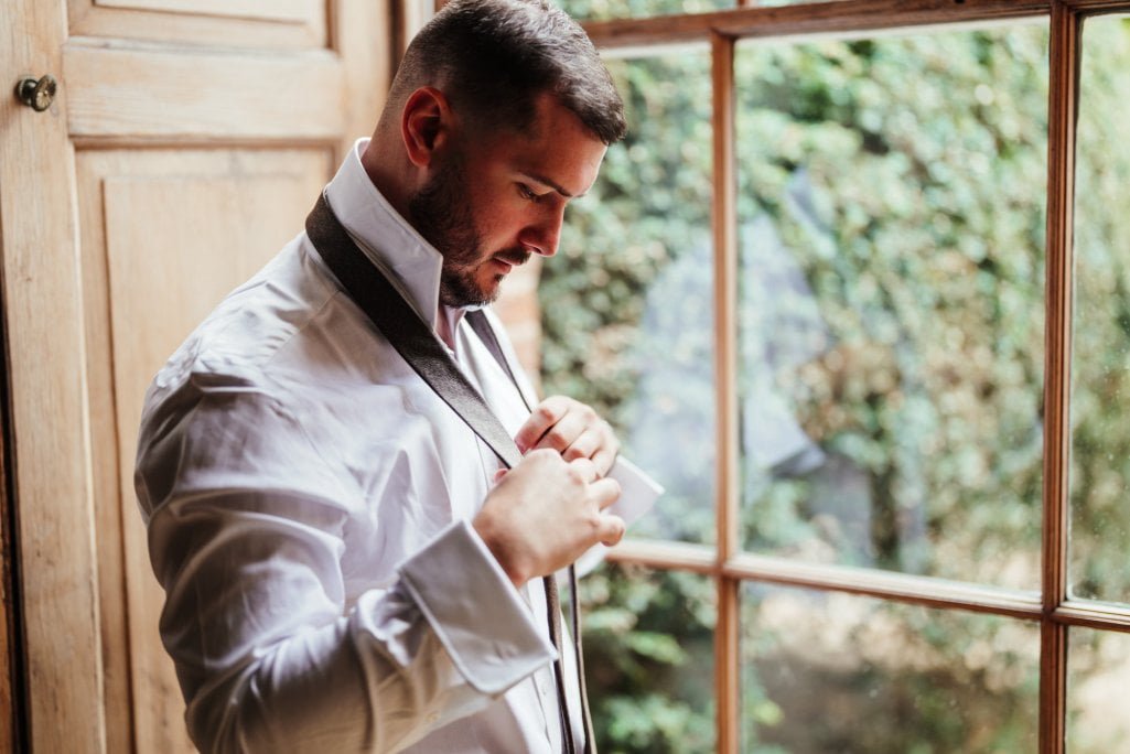Man adjusting tie by window, elegant attire.