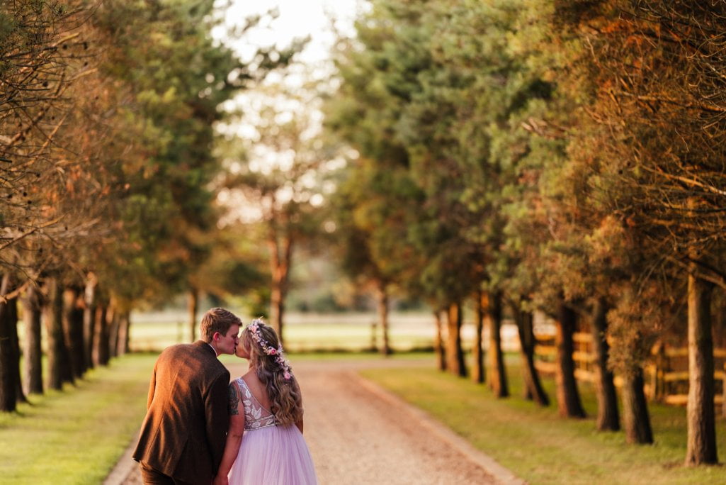 Couple kissing on a tree-lined path at sunset.